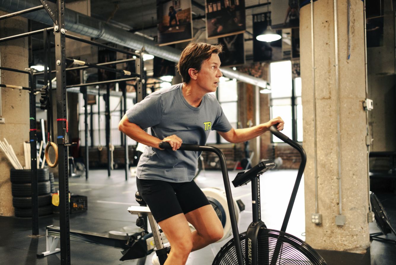 Member pushing hard on an assault bike on the gym floor