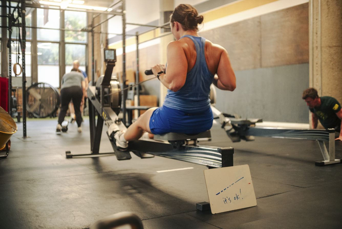 Member on the rower during class with an it's ok sign propped in front